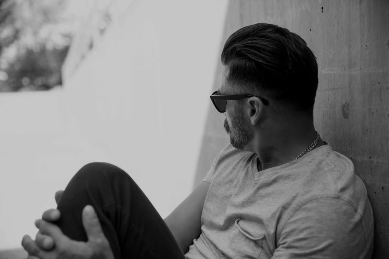 A photo of a man wearing sun glasses, leaning against a concrete wall.